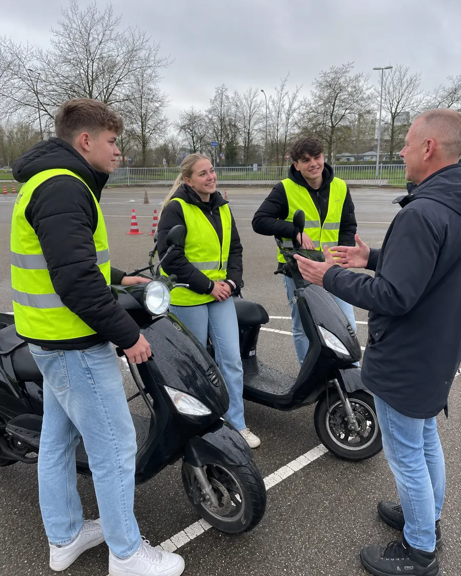 Instructeur geeft uitleg aan drie leerlingen bij hun lesscooters